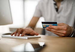 Person holding credit card while typing on computer