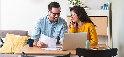 smiling man and woman with paperwork and laptop at table