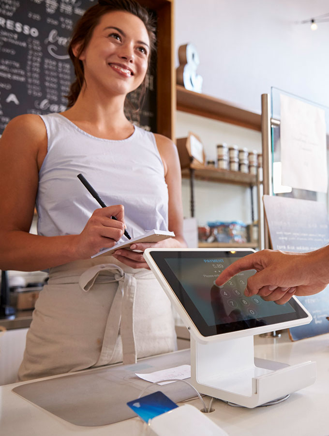 Cafe worker smiling at someone as they pay via a tablet.